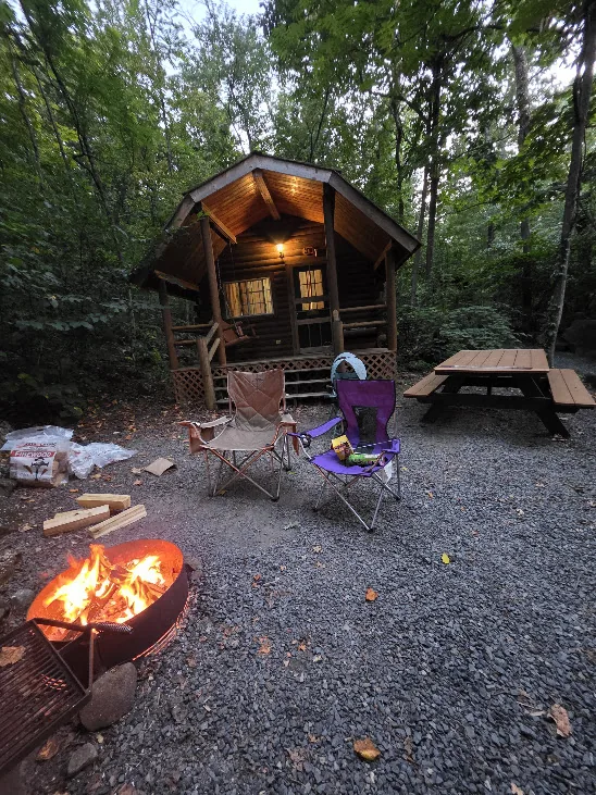 Campfire burning outside a small wooden cabin at a wooded campsite at dusk