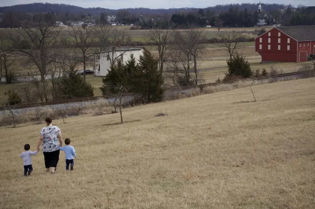 Matt’s wife and twin sons walking hand in hand down a grassy hill toward a red barn in Gettysburg