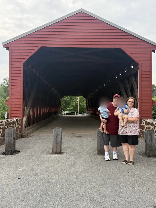 Matt with his wife and twin sons in front of a red covered bridge in Gettysburg